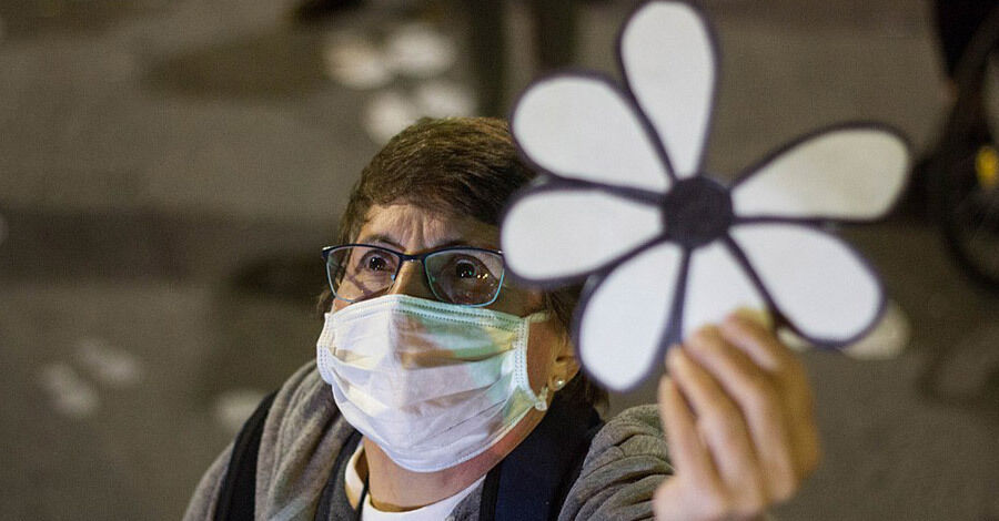 Señora de tapabocas levantando una margarita a la cual le falta un pétalo y representa a los desaparecidos en época de dictadura